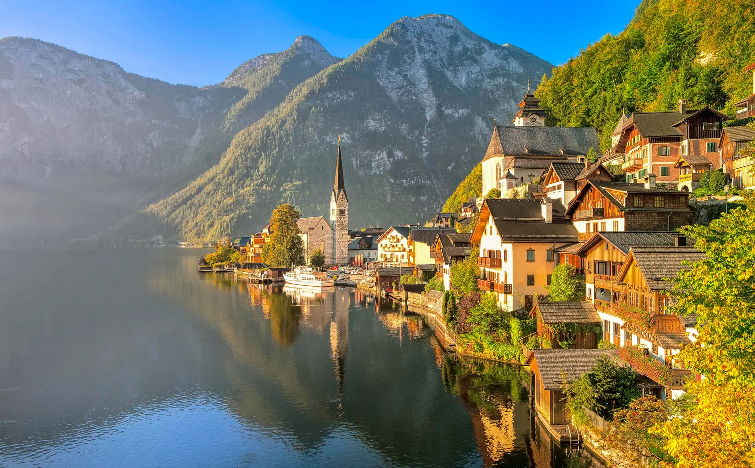 Hallstatt village and its church spire reflected in the Hallstätter See, with the Dachstein mountains behind